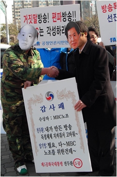 ▲ '5공과 MBC의 만남'이라는 주제로 진행된 퍼포먼스에서 가면을 쓴 가짜 전두환 전 대통령이 가짜 엄기영 MBC 사장에게 감사패를 전달하고 있다. ⓒ뉴데일리