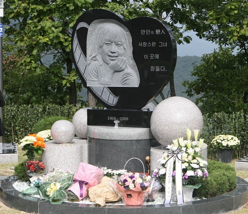 ▲ 고인의 얼굴을 음각으로 새긴 하트모양의 조각상이 고 최진실의 유골함이 묻힌 원형 묘분 위에 세워진 가운데 조문객들이 놓고 간 조화들이 묘분 위를 장식하고 있다.&nbsp; ⓒ 뉴데일리