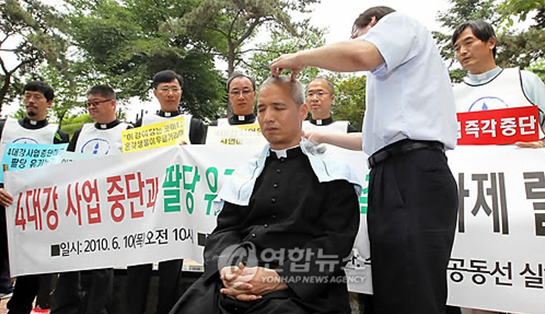 ▲ 천주교 수원교구 공동선실현사제연대, 의정부사제연대 소속 신부 등이 벌인 사제삭발식. 플래카드 등엔 팔당유기농 농가가 피해를 본다는 취지의 내용이 있다. 강을 살리자며 4대강을 반대하면서 대표적인 유기물 오염원인 농경지를 언급하는 것이 아이러니하다. ⓒ 뉴데일리