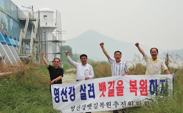 ▲ 영산강뱃길복원 운동을 펼치는 시민들이 영산포등대 근처에서 뱃길복원을 호소하고 있다. 옆엔 한길이나 자란 풀숲이 가득안 강변. ⓒ 뉴데일리