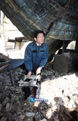 ▲ 지난 26일 연평도를 방문한 김문수 경기지사가 폐허가 된 집안에서 불에 탄 재봉틀을 들어보이고 있다.ⓒ경기도 제공