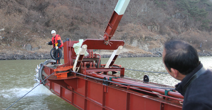 ▲ 준설선 흡입구가 쓰레기를 떼내기위해 수면 위로 들어올려져 있다. 작업자가 타이어를 먼저 떼내고 다른쓰레기를 떼기위해 조종기사에게 작동신호를 보내고 있다.