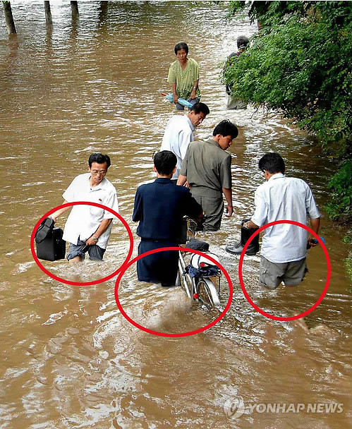▲ 미국 AP통신이 18일 디지털 기술 조작을 의심해 고객에게 삭제를 당부한 북한의 대동강변 수해 사진. 문제의 사진은 북한 조선중앙통신이 15일 촬영해 16일 계약사인 AP통신 등에 전송했다. 해당 사진은 폭우로 대동강 주변 도로가 완전히 침수된 상황에서 주민 7명이 걸어가는 장면을 담고 있다. 사진에는 도로에 성인의 무릎 높이 이상으로 물이 차 있는 것으로 나타나있다. 북한 관련 웹사이트인 노스코리아테크(www.northkoreatech.org)는 "비전문가적 관점에서 보면 AP통신의 편집인들은 사진이 포토샵으로 처리된 것으로 의심하고 있다"고 설명하며 사진이 조작된 근거로 침수도로를 보행하는 주민들의 다리 부분(붉은 선)이 깔끔하고 바지에 흙탕물이 튄 부분이 적다는 점을 들었다.