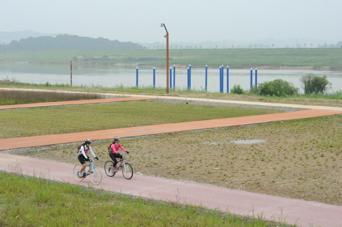 ▲ - 행복1공구 좌안 금남제에 설치된 마리나(보트선착장) 옆을 자전거동호인 최연희씨(앞)와 이미란씨(뒤)가 자전거를 타고 달리고 있다.ⓒ