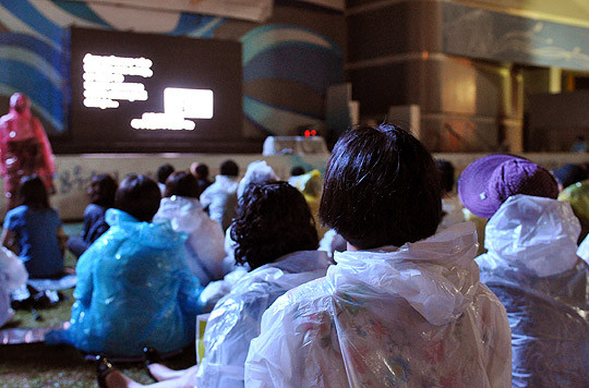 ▲ 비를 맞으며 '김정일리아' 영화를 보는 참석자들.(뉴데일리 추진혁 기자)