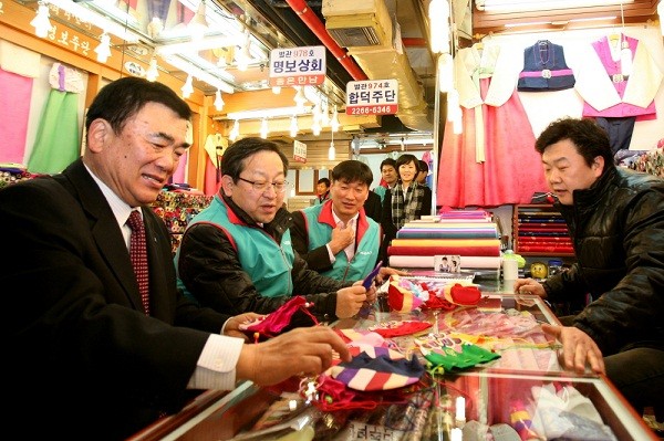 ▲ 하나은행 김종준 은행장(좌측 가운데)과 김창근 노조위원장(좌측 세번째)이 5일 임직원 100여명과 함께 서울의 대표적인 전통시장인 종로구 광장시장을 방문해 금융 애로사항을 듣고 서민지원 상품을 상담을 했다. 광장시장 방문중 광장시장 상인 총연합회 윤영재 회장(좌측 첫번째)과 함께 한복을 파는 상가(사장 맹영권) 에 들러 애로사항을 듣고 복주머니를 구입하고 있다.