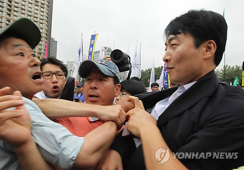 ▲ 지난해 7월3일 서울시청 앞 광장에서 열린 농어민대회에서 통합진보당 이석기 의원이 "빨갱이가 왜 여길 왔느냐"고 비판하는 한 농민에게 멱살을 잡히고도 미소를 짓고 있다. ⓒ연합뉴스