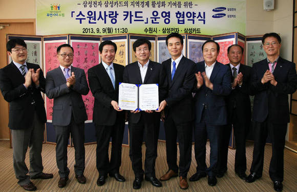 ▲ 삼성전자는 9일 수원 화성행궁 내 수원시장 집무실에서 염태영 수원시장(사진 왼쪽에서 네번째), 한민호 삼성전자 수원지원센터장(전무)(사진 왼쪽에서 세번째), 황일 삼성카드 전략영업담당 상무(사진 오른쪽에서 네번째)가 참석한 가운데 '지역사회 경제활성화를 위한 MOU'를 체결했다.