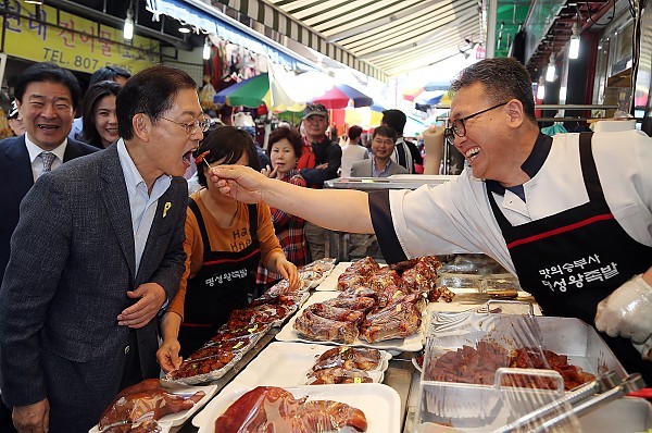 ▲ 김황식 전 총리가 6일 시흥 현대시장에서 한 상인이 건넨 족박을 받아 먹고 있다. ⓒ 김황식 선거캠프 제공