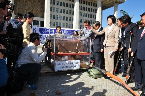 ▲ 국회 환노위원들이 16일 국회본관 계단 앞에서 진행한 싱크홀 실험에서 토사 유출이 너무 더디자, 관계자들이 배수구의 철망을 인위적으로 제거하고 있다. ⓒ뉴데일리 이종현 기자