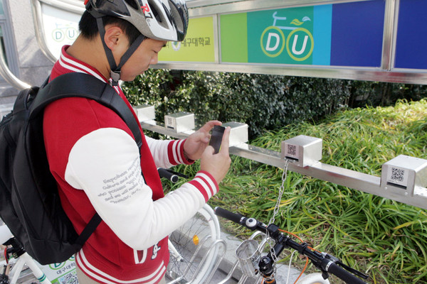 ▲ 한 대구대 학생이 DU바이크 거치대에서 스마트폰 앱을 이용해 자전거를 대여하고 있다.ⓒ대구대 제공