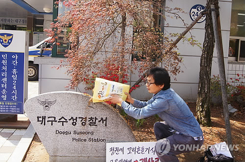 ▲ 21일 대구 수성경찰서 앞에서 박성수(42)씨가 개사료를 뿌리고 있다. 박씨는 이날 오전 박근혜 대통령을 비방하는 유인물을 제작한 혐의(출판물에 의한 명예훼손)로 조사를 받기 위해 경찰서를 찾았다. 50여 분간의 조사 도중 박씨는 "더는 조사를 못 받겠다"며 경찰서 밖으로 나와 정문 앞 팻말에 미리 준비한 5㎏짜리 개 사료 일부를 쏟아부었다. ⓒ 연합뉴스