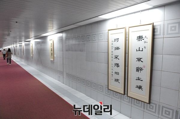 ▲ 새정치민주연합 문희상 의원의 [태산불양토양] 서예 작품이 걸려 있는 국회본청~의원회관 사이의 지하통로. 국회 보좌진들이 문희상 의원의 서예 작품을 뒤로 하고 발걸음을 옮기고 있다. ⓒ뉴데일리 이종현 기자