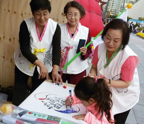 코엑스 광장 체험장에서 1회용 한복을 입고 애국가 식탁보 그리기 행사에 참여한 김정자 회장(가운데) 최재숙 박사(오른쪽) 등 미래여성네트워크 회원들 ⓒ뉴데일리