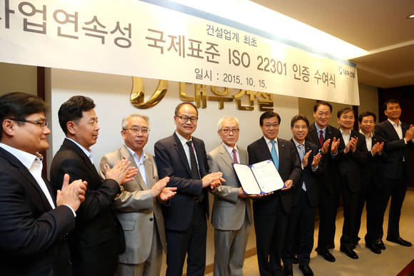 ▲ 지홍근 대우건설 HSE-Q 실장(오른쪽)과 천정기 BSI Korea 회장이 ISO 22301 인증패를 들고 관계자들과 기념촬영을 하고 있다.ⓒ대우건설