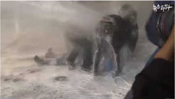 ▲ 빨간 우의를 입은 남자가 누워있는 백남기씨를 덮치기 직전의 사진. 그는 멀리서 접근해 그의 위에 올라탔다. ⓒ뉴스타파