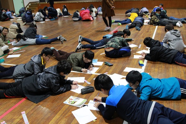 ▲ 제천영재캠프에 참여한 학생들이 제천청소년수련원 체육관 마루바닦에 엎드려 주어진 과제를 풀고 있다ⓒ제천교육지원청