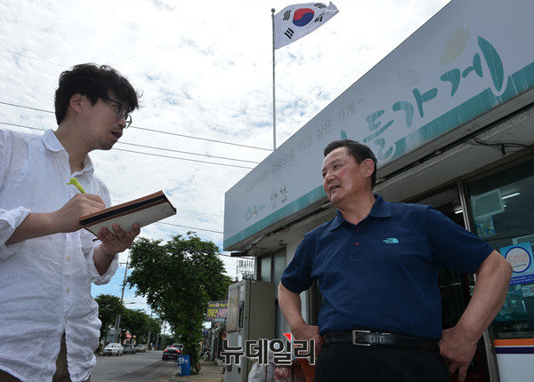 ▲ 강정마을 5거리에서 슈퍼를 하는 강희상씨 모습. 그의 가게에는 찬성의 표시로 태극기가 걸려있다. 반대파는 구호가 쓰여있는 노란색 깃발이 걸려 있다.ⓒ뉴데일리 정상윤 사진기자