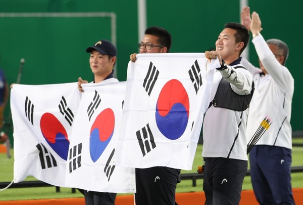 2016 리우올림픽 남자양궁 단체전 결승에서 금메달을 차지한 한국 대표팀의 구본찬(오른쪽부터), 김우진, 이승윤이 태극기를 들고 관중에게 인사하고 있다.ⓒ연합뉴스