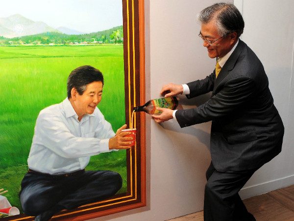 ▲ 더불어민주당 문재인 전 대표가 환하게 웃으면서 고인이 된 노무현 전 대통령이 술잔을 내밀고 있는 형상에 막걸리를 따르는 포즈를 취하고 있다. ⓒ뉴시스 사진DB