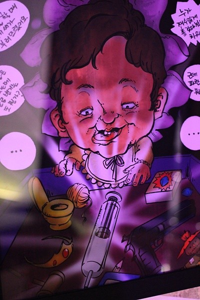 ▲ 벙커원에 전시되고 있는 박근혜 대통령 풍자 그림. 돌잡이를 하고 있는 박근혜 대통령을 풍자한 그림으로 주사기, 권총 등이 돌잡이 상에 올라와 있다. ⓒ뉴데일리 강유화 기자