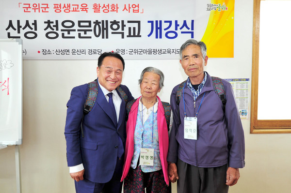 ▲ 김영만 군위군수(왼쪽)가 10일 운산리 마을회관에서 청운문해학교 교육생과 함께 가방을 메고 활짝 웃고 있다.ⓒ군위군