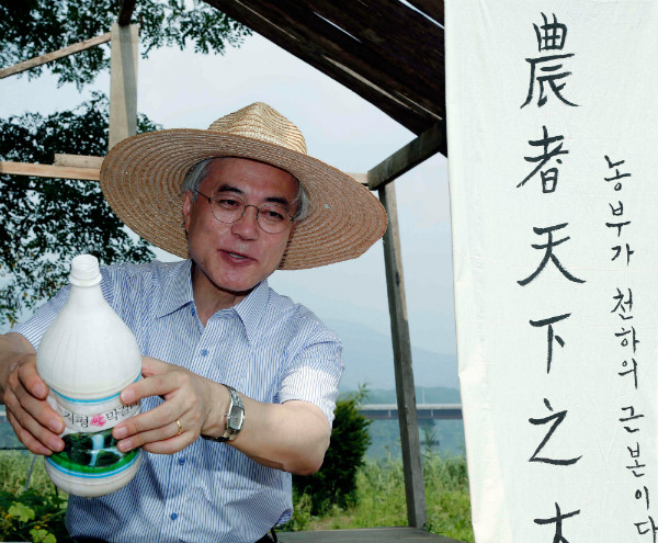 ▲ 문재인 대통령이 지난 2012년 대선 과정에서 경기도 양평의 농경지를 찾아 밀짚모자를 쓰고 논의 잡초를 뽑은 뒤 막걸리를 나누고 있다. 농자천하지대본이라는 글귀가 옆에 보인다. ⓒ뉴시스 사진DB