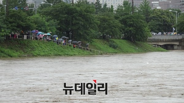 ▲ 16일 오전 집중호우로 충북 청주 무심천이 한때 범람위기상황까지 수위가 올라오자 청주시민들이 무심천에서 불어난 물을 걱정스럽게 바라보고 있다.ⓒ김정원기자