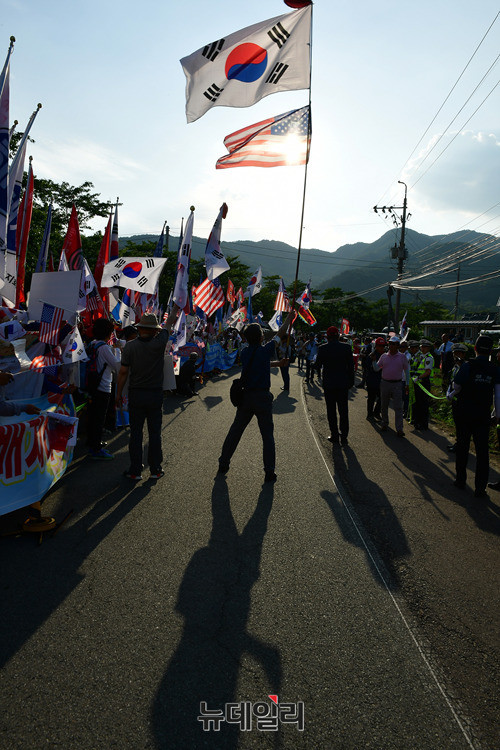사드배치 촉구를 요구하는 한 집회 참가자가 지난 6월 22일 성주 사드포대 기지 입구가 위치한 경북 성주군 소성리마을회관 앞에서 태극기와 성조기를 단 깃발을 흔들고 있다. ⓒ뉴데일리