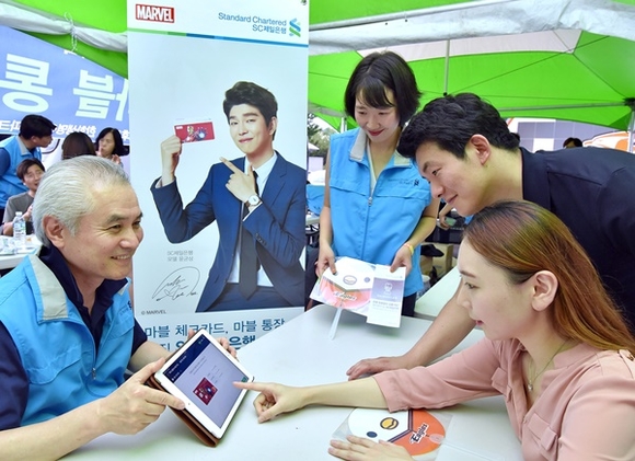 ▲ 박종복 SC제일은행장(왼쪽)이 지난 10일 대전 한화생명이글스파크에서 야구장을 찾은 관중에게 태블릿PC를 이용해 상품 가입 절차를 설명하고 있다. ⓒSC제일은행