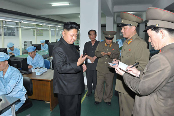 ▲ "이거 국제전화 되나?" "당연히 안 됩니다." 5.11공장을 찾아 북한제 휴대전화를 보는 김정은. ⓒ北선전매체 화면캡쳐.