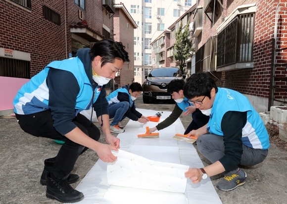▲ 지난 22일 서울 마포구에서 임직원들이 노후주택에 도배할 벽지에 풀을 바르고 있다.ⓒ대우건설