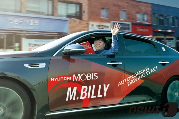 ▲ 서산주행시험장내 도로에서 자율주행차 M.BILLY를 테스트하는 연구원이 책을 보며 밖으로 손을 흔들고 있다.ⓒ현대모비스