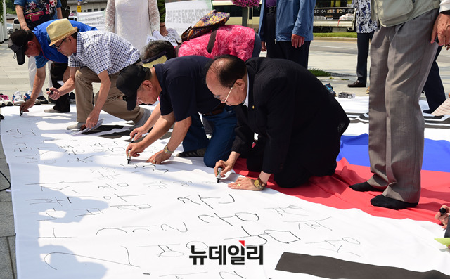 ▲ 납북자 가족들이 가로 6.8m 길이의 대형 태극기에 가족들의 이름을 쓰고 있다. 6.8m의 길이는 6·25 전쟁 68주년을 기념하기 위한 것이다. ⓒ뉴데일리 이종현