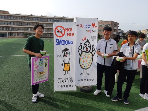 ▲ 운호중 학생들이 29일 운동장에서 주먹밥을 받아 들고 ‘사랑 뿜뿜’ 주먹밥 DAY 행사와 금연 캠페인 안내 피켓 앞에서 즐거워하고 있다.ⓒ운호중