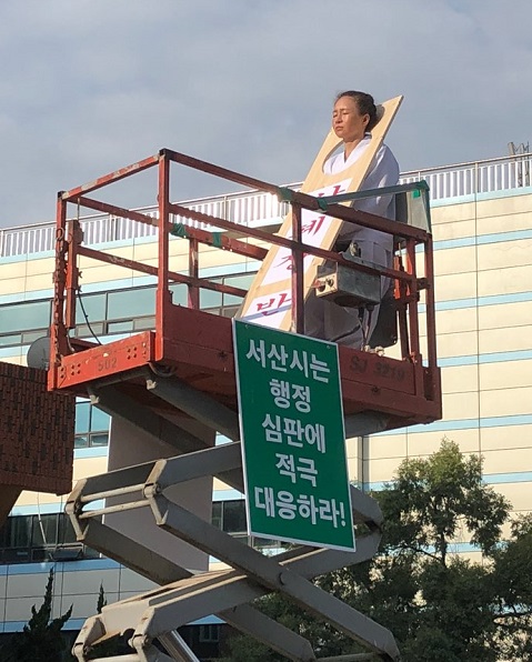 ▲ 산폐장반대오스카빌대책위 한석화 위원장이 하얀 소복을 입고 목에 씌우는 형구인 칼을 쓰고 고소작업대 위에 올라 시위를 하고 있다.ⓒ서산태안환경운동연합