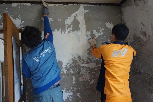▲ 포스코건설 직원과 소방대원이 노후된 벽지를 교체하는 모습. ⓒ포스코건설