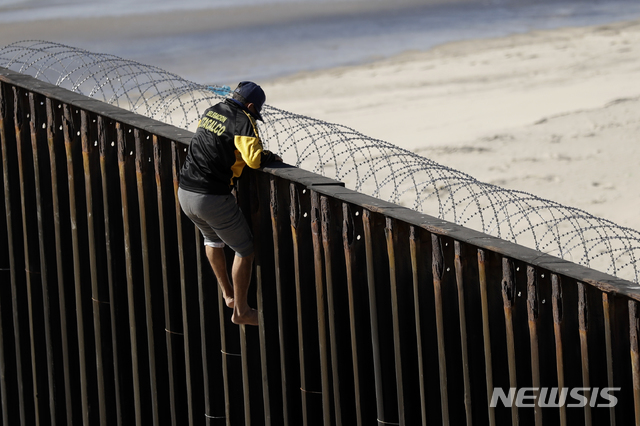 ▲ 미국과 멕시코 국경을 막고 있는 구조물 위에 한 남성이 올라가 있다ⓒ뉴시스. 무단 전재 및 재배포 금지.