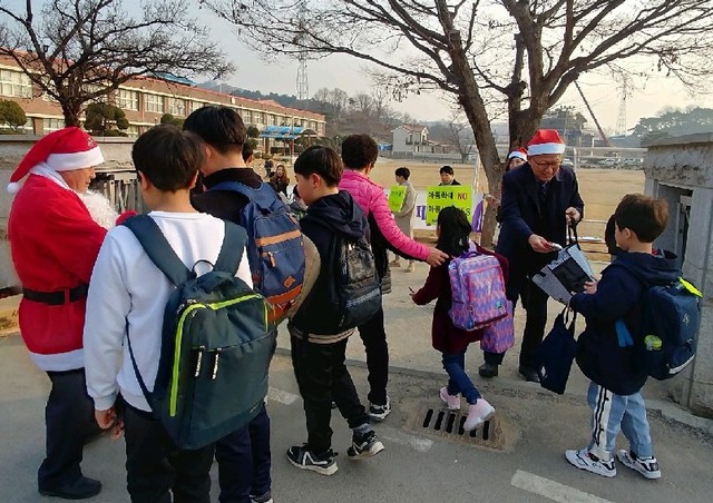 ▲ 유경균 제천교육장(오른쪽)이 11일 홍광초등학교에서 산타복장을 하고 등교하는 학생들에게 덕담과 함께 간식을 나눠주고 있다.ⓒ제천교육지원청