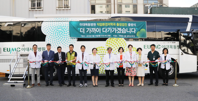 ▲ 문병인 이화여자대학교 의무부총장 겸 의료원장(사진 왼쪽에서 일곱 번째), 한종인 이대목동병원장(사진 왼쪽에서 여덟 번째), 김현주 이대목동병원 직업환경의학과장 등을 비롯한 경영진이 출장검진 출정식에서 테이프 커팅식을 진행하고 있다. ⓒ이대목동병원
