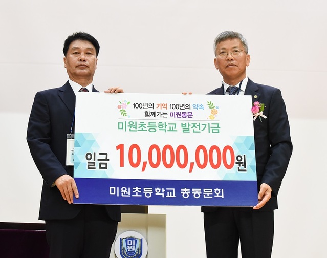 ▲ 이상돈 미원초 총동문회장이 19일 미원초에서 열린 개교 주년 기념식에서 박준영 미원초 교장에게 1000만원의 장학기금을 전달하고 있다.ⓒ미원초 총동문회