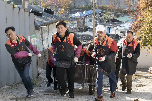 ▲ 지난 7일 서울 노원구 104마을에서 최신원 회장이 구성원들과 함께 연탄을 실은 손수레를 끌며 언덕을 오르는 모습.ⓒSK네트웍스