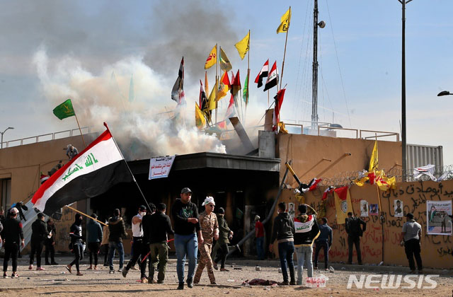 ▲ 이라크 주재 미국대사관 입구와 담장을 파괴한 뒤 환호하는 시위대. 이들이 흔드는 깃발 가운데는 이라크 국기 외에도 헤즈볼라, 카타이브 헤즈볼라, 인민동원군 등 시아파 무장조직 깃발들이 보인다. ⓒ뉴시스 AP. 무단전재 및 재배포 금지.