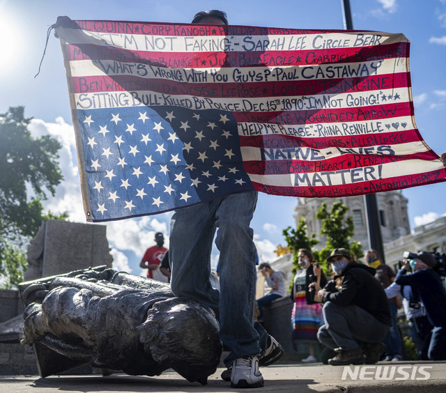 ▲ [세인트폴=AP/뉴시스]10일(현지시간) 미 미네소타주 세인트 폴의 미네소타주 의사당에서 경찰에 살해된 원주민들의 이름이 쓰인 미국 국기를 든 한  남성이 쓰러져 있는 크리스토퍼 콜럼버스 동상의 목을 무릎으로 누른 채 시위하고 있다. 2020.06.11.
ⓒ뉴시스