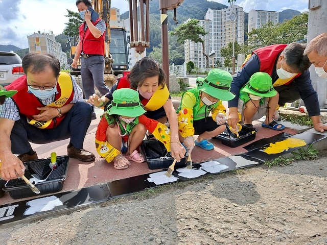▲ 괴산읍 주민자치위원들과 어린이집 학부모, 어린이가 18일 읍내 도로 경계석에 ‘양옆을 살펴요 #괴산사랑’을 그리고 있다.ⓒ괴산군
