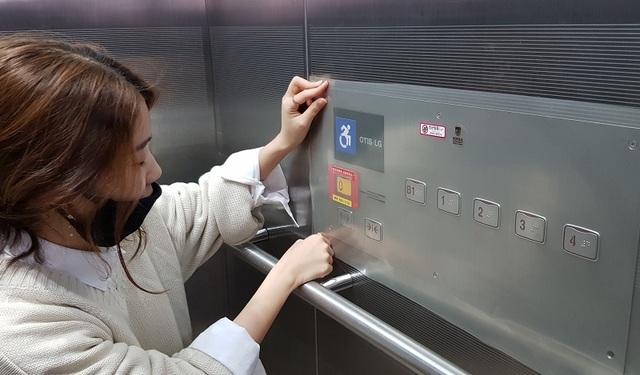▲ 한 여성이 엘리베이터에 코로나19 방역을 위해 숫자 버튼 위에 방역필름을 붙이고 있다.ⓒ충북도