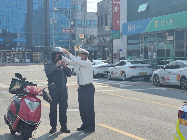 ▲ 한 경찰이 오토바이 운전자에게 안전모 착용방법을 가르쳐 주고 있다.ⓒ충남경찰청
