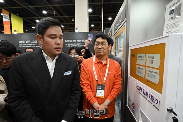 ▲ 정 부회장이 스마트 담배 자판기 성인인증 방법과 소비 수요에 대해 설명을 듣고 있다ⓒ사진=공동취재단