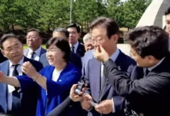 ▲ 2022년 2월 대선 후보였던 이재명 더불어민주당 대표가 제주 4·3평화공원을 찾았다. 참배 후 기자회견에서 박찬대 민주당 의원이 이 대표의 코딱지를 빼내주는 듯한 모습이 포착됐다. ⓒ온라인 커뮤니티 캡쳐.