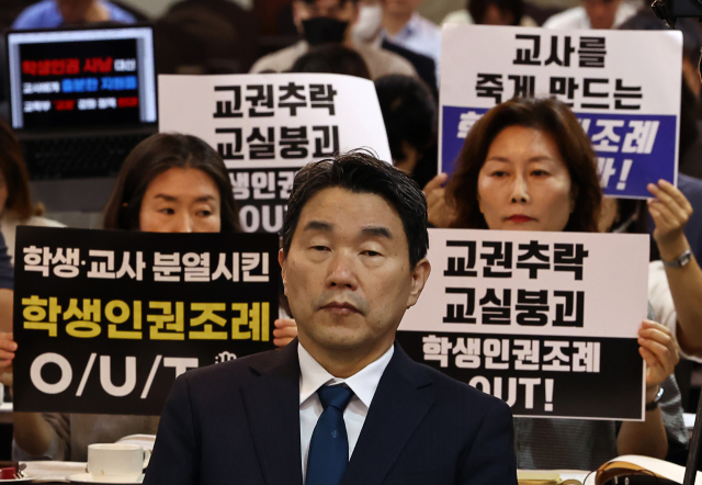 ▲ 지난 8월 10일 서울 코리아나호텔에서 열린 '교권 회복 및 보호를 위한 교육부-국가교육위원회 공동주최 토론회'에서 서울교육사랑학부모연합 등 단체가 학생인권조례 폐지를 촉구하는 피켓을 들고 있다. 앞은 이주호 부총리 겸 교육부 장관. ⓒ연합뉴스